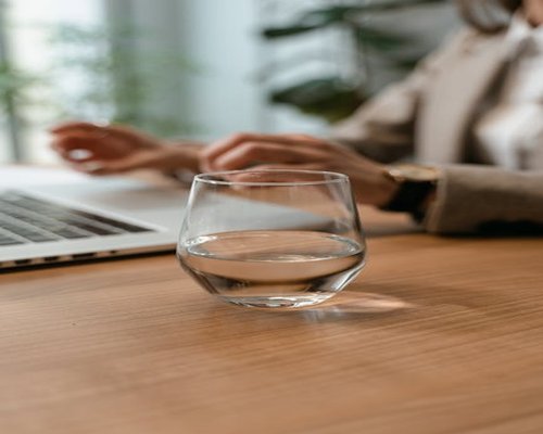 A glass of water on a modern desk next to a laptop